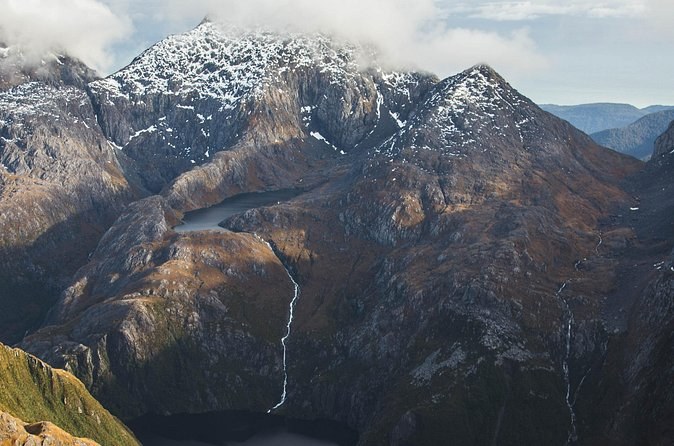 Bare rock ridges dusted with snow and a thin waterfall, seen from the air