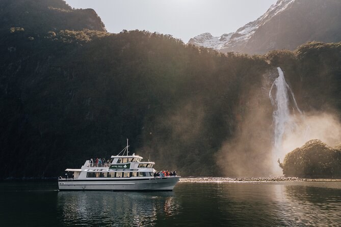 A cruise boat below a waterfall, spray drifting across the cliff face