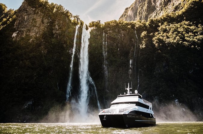 A cruise boat under twin waterfalls in low evening light