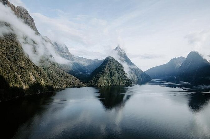 Cloud lifting off steep green peaks, their reflections in still water