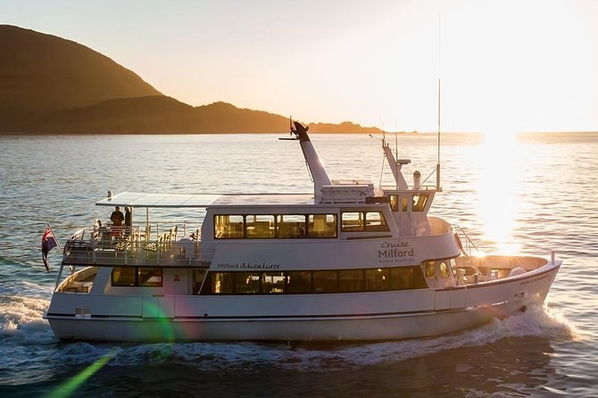 A cruise boat crossing the fiord at sunset, the sun low over the ridge