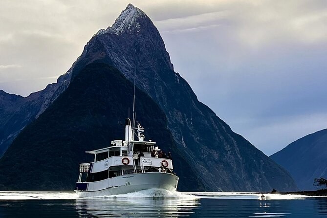 A cruise boat heading out below a steep, pyramid-shaped peak