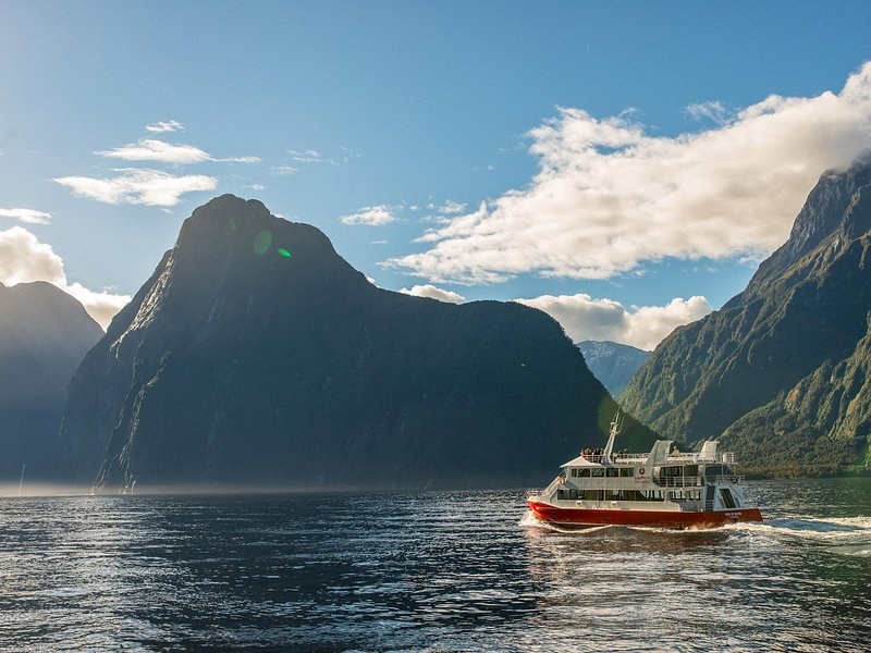 A red and white cruise boat crossing below a dark peak as the cloud clears