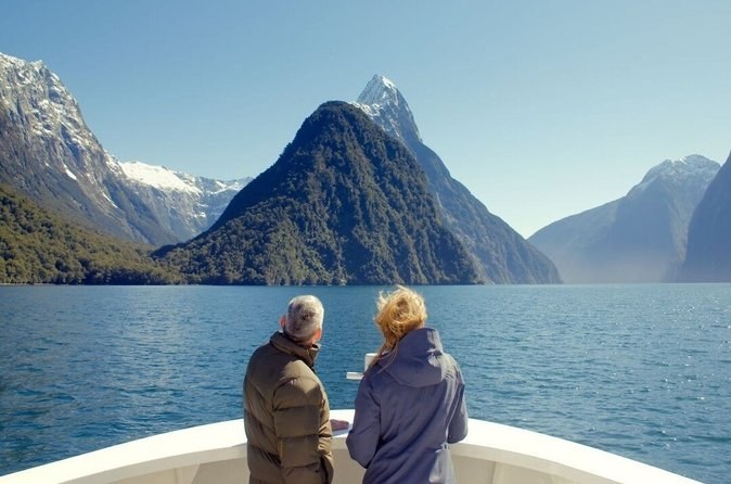 Two passengers at the bow, seen from behind, looking at a pointed peak across the water