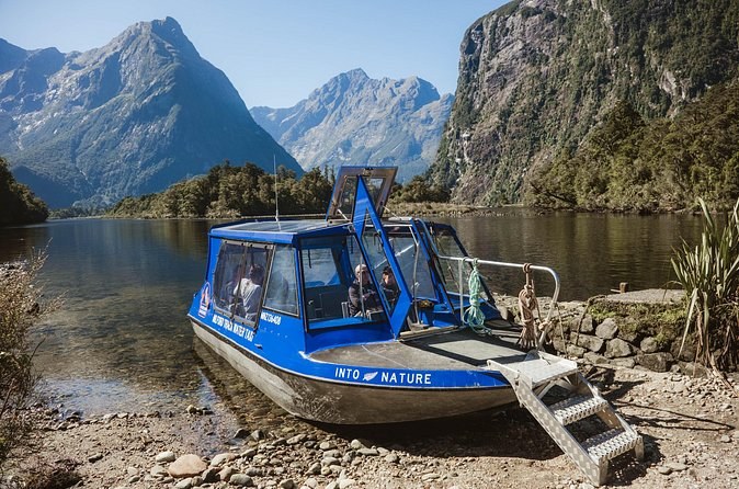 A blue water taxi pulled up on a stony shore below forested peaks
