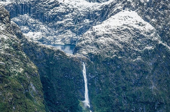 A long waterfall falling into a snow-dusted valley, seen from the air